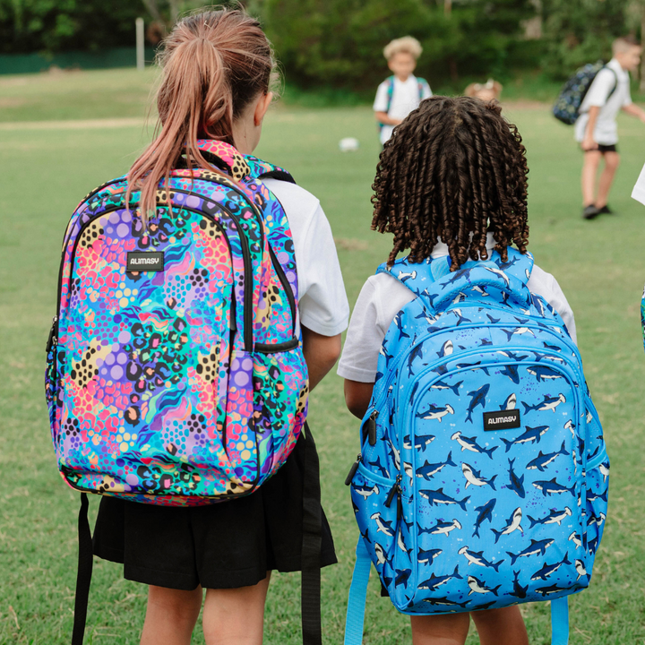 Two children with patterned colourful backpacks on a grassy field