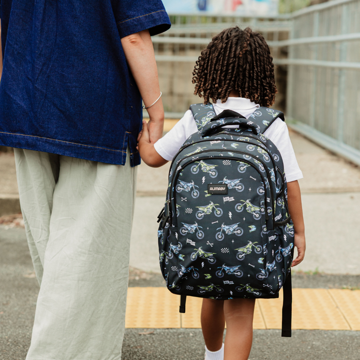 Child with a motorbike backpack holding hands with an adult, walking outdoors.
