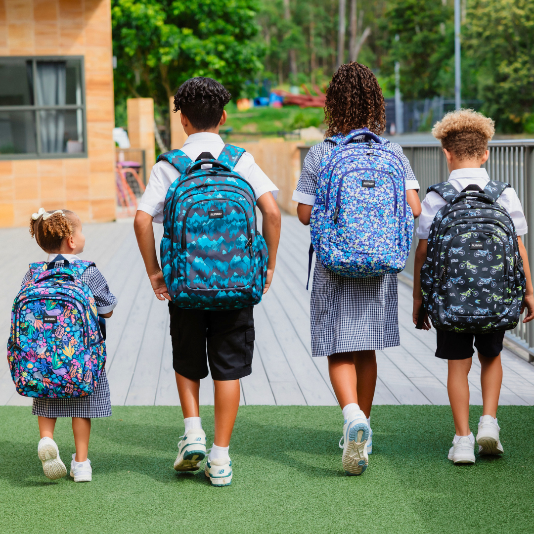 Four children wearing colourful backpacks walking together outdoors.