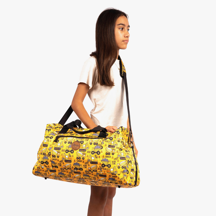 girl wearing alimasy yellow construction print kids duffle overnight bag across body